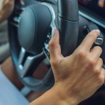 Ręka kobiety przełącza płaty selektora biegów na kierownicy Ręka przełącza dźwignię zmiany biegów samochodu zbliżenie strzałki ręcznej zmiany biegów na kierownicy samochodu