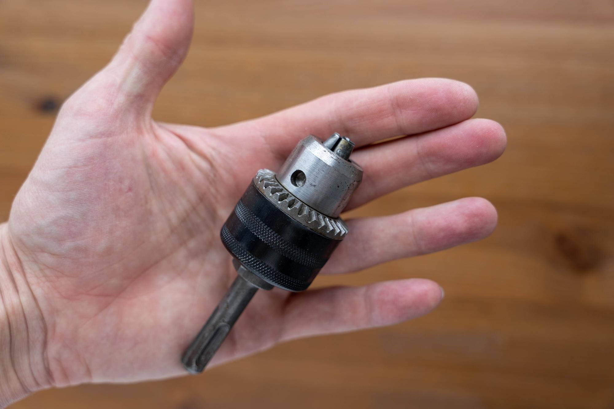 Ręka mężczyzny trzyma wiertło na drewnianym tle