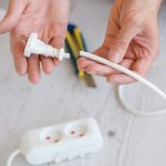 Bliska elektrycznego przedłużacza europejskiego, listwy zasilającej i gniazd, męskie ręce elektryka trzymają przecięty przewód kablowy