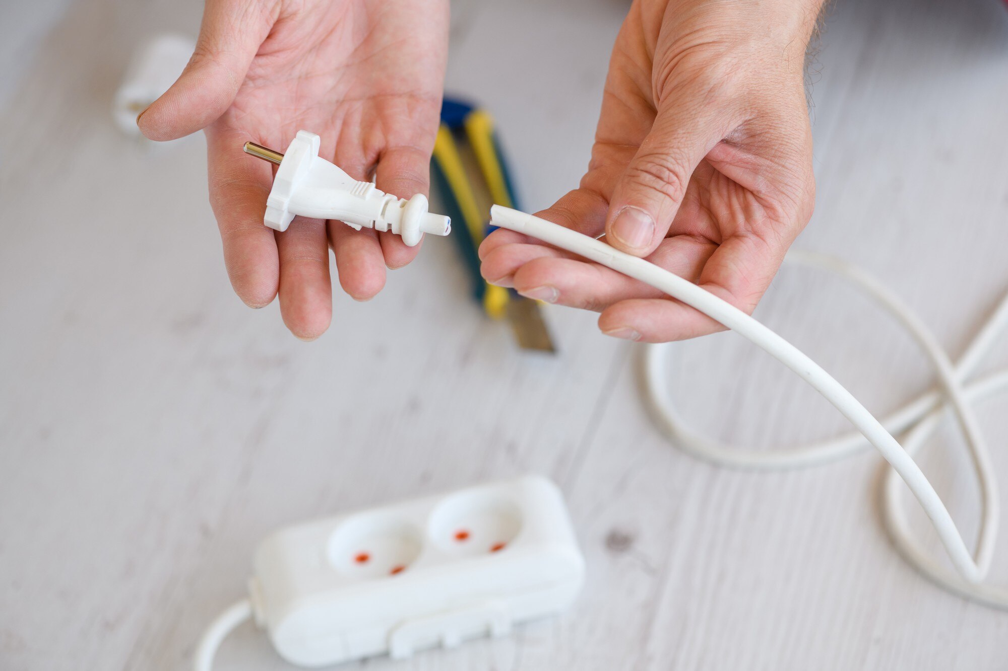 Bliska elektrycznego przedłużacza europejskiego, listwy zasilającej i gniazd, męskie ręce elektryka trzymają przecięty przewód kablowy