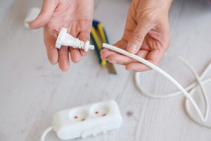 Bliska elektrycznego przedłużacza europejskiego, listwy zasilającej i gniazd, męskie ręce elektryka trzymają przecięty przewód kablowy