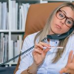 Zbliżenie niezmotywowanej blond sekretarki polerującej paznokcie w miejscu pracy podczas rozmowy przez telefon