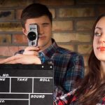 Zamknij się młoda biała kobieta z deską klapy, patrząc na lewą stronę, przed męskim fotografem robienia zdjęć.