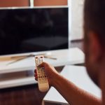 Widok z tyłu człowieka trzyma w ręku pilota zdalnego sterowania i włączania telewizora.