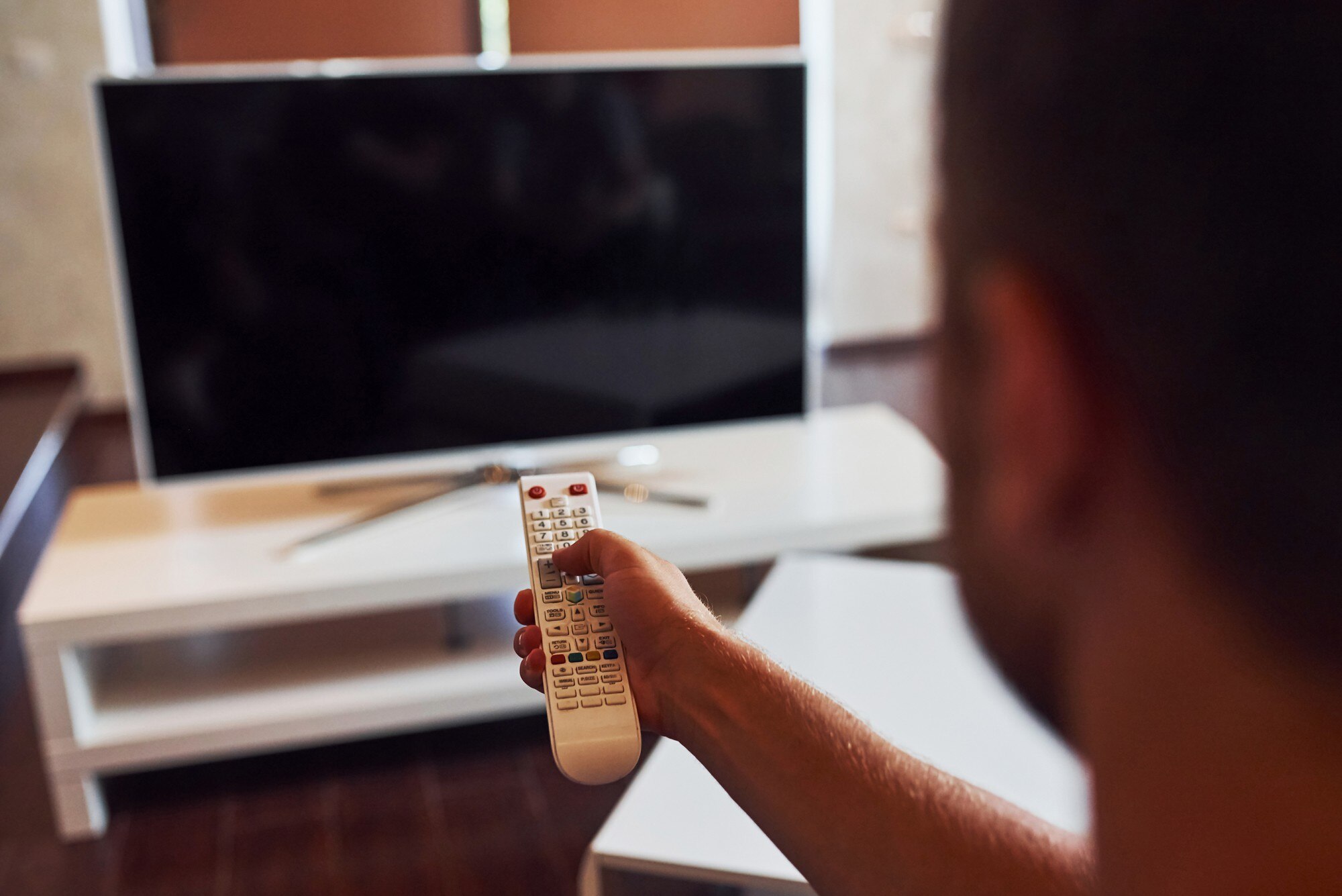 Widok z tyłu człowieka trzyma w ręku pilota zdalnego sterowania i włączania telewizora.