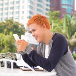 Młody człowiek pijący kawę w kawiarni i patrzący na ekran telefonu