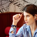 Zamyślona młoda kobieta słucha muzyki w słuchawkach i zastanawia się nad pomysłami na nowy projekt, siedząc przy kawiarnianym stoliku