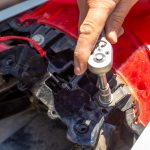 Naprawa i demontaż motocykla. Mężczyzna odkręca łączniki bagażnika kluczem nasadowym.