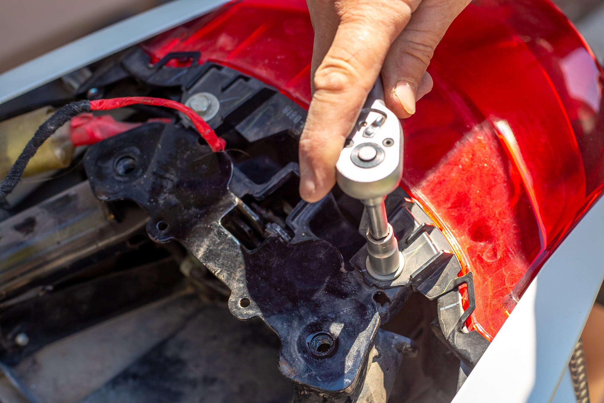 Naprawa i demontaż motocykla. Mężczyzna odkręca łączniki bagażnika kluczem nasadowym.