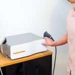 Profesjonalny masażysta obok innowacyjnej maszyny fal uderzeniowych w klinice