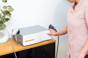 Profesjonalny masażysta obok innowacyjnej maszyny fal uderzeniowych w klinice