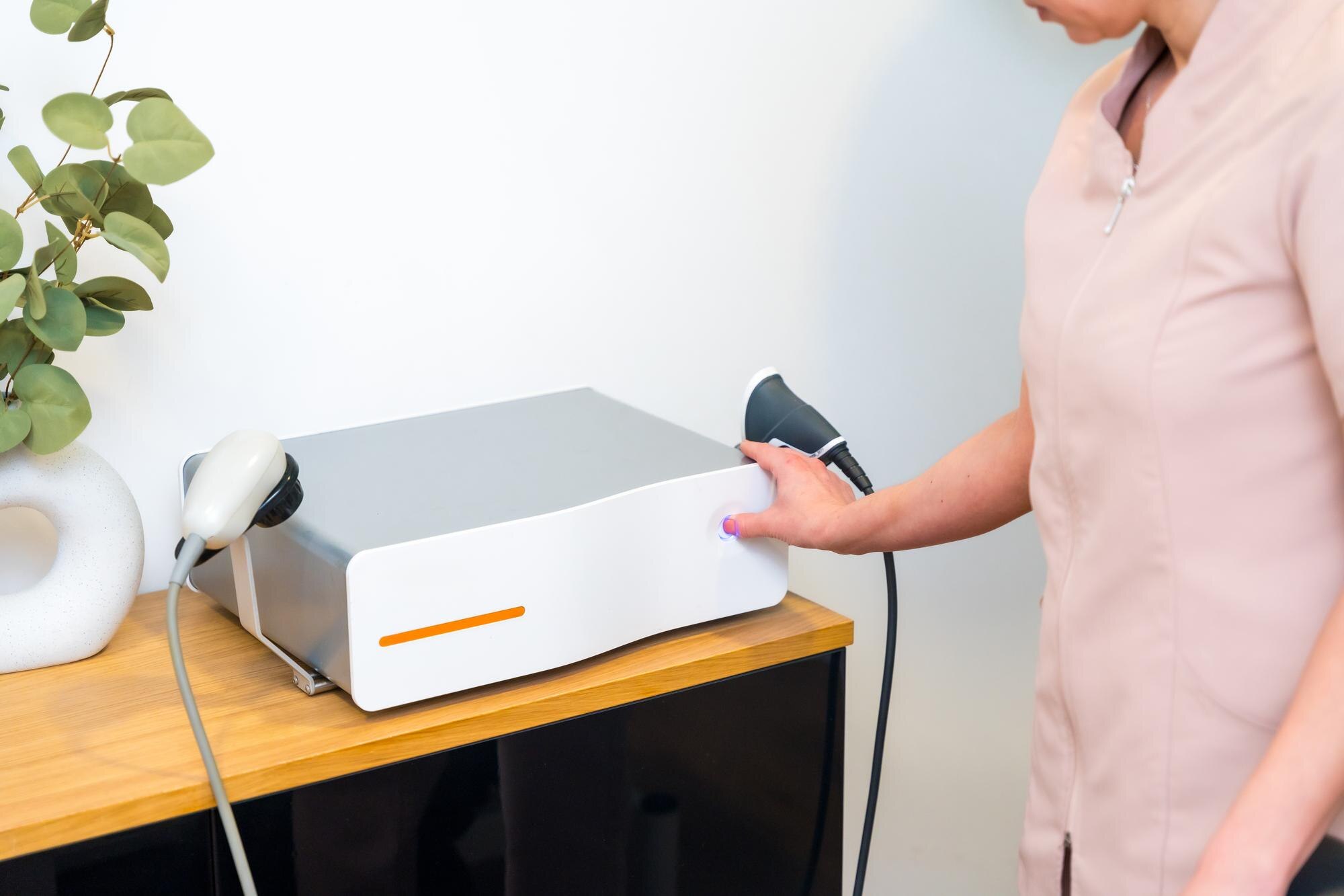 Profesjonalny masażysta obok innowacyjnej maszyny fal uderzeniowych w klinice