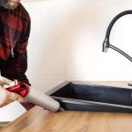 Mężczyzna instaluje czarny kamień do zlewu w kuchennym blacie Pracownik uszczelnia zlew kuchenny za pomocą uszczelniacza za pomocą pistoletu uszczelniania konstrukcyjnego