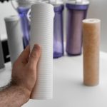 Człowiek trzymający w ręku czysty filtr do odwróconej osmozy do oczyszczania wody na stole w kuchni