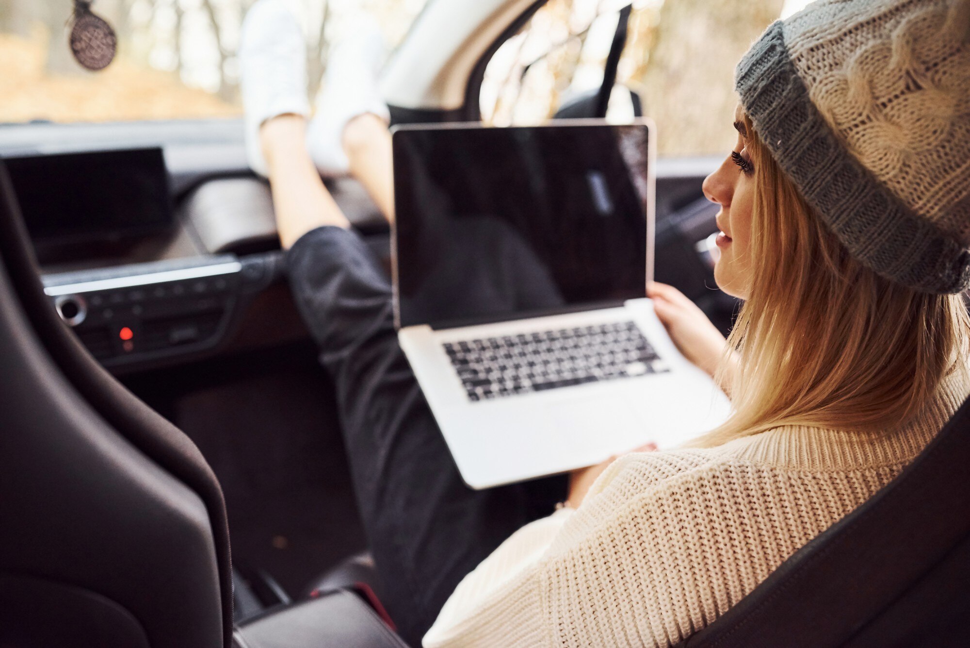 Siedzi z laptopem i filiżanką napoju. Dziewczyna ma jesienną podróż samochodem. Nowoczesny, nowy samochód w lesie.