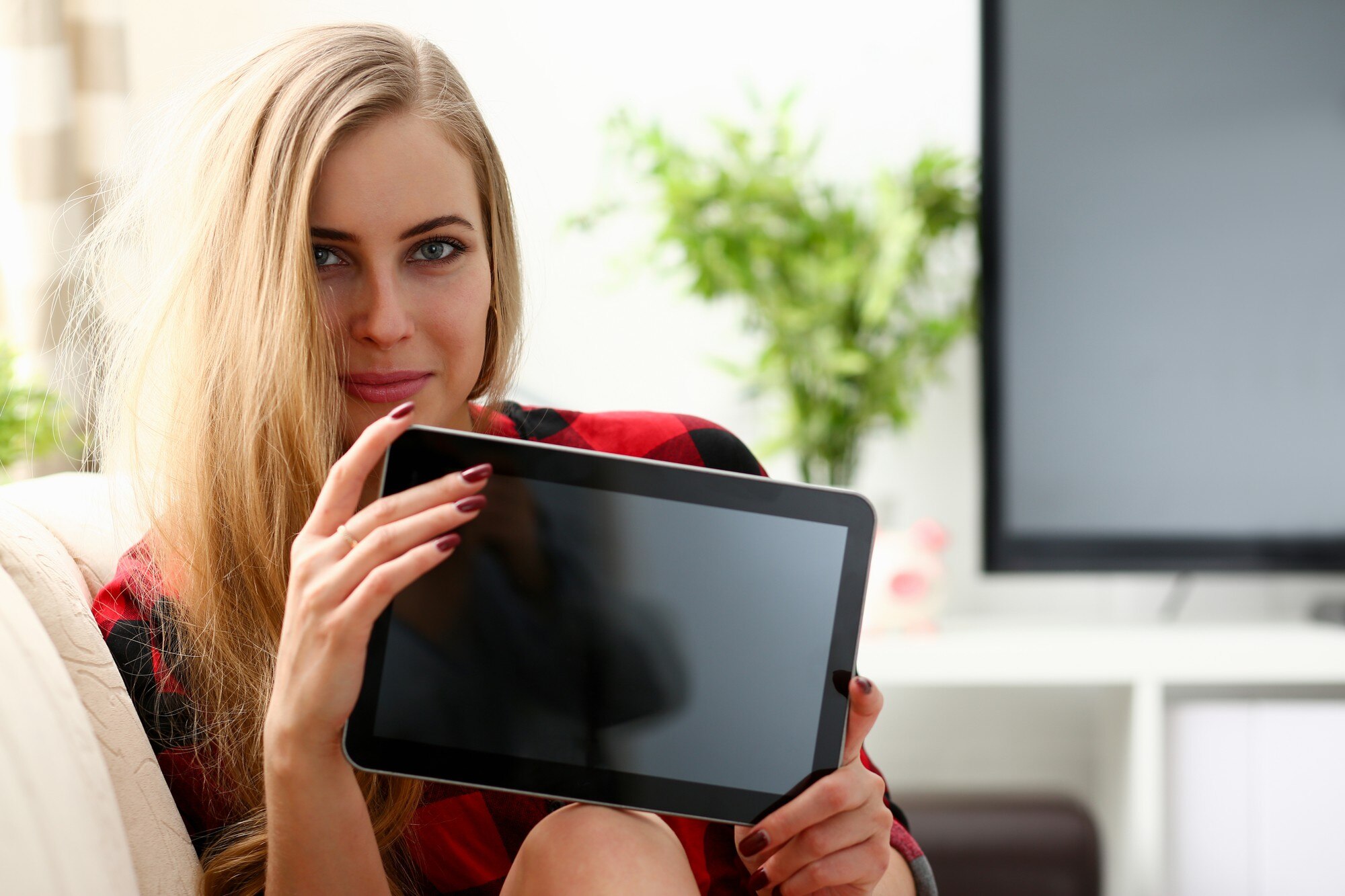 Ładna blond młoda kobieta trzyma laptopa w ramionach siedzi na kanapie