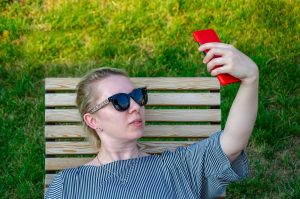 Blondynka robi sobie selfie, robi zdjęcie lub komunikuje się przez wideorozmowę przez telefon w słoneczny dzień w parku