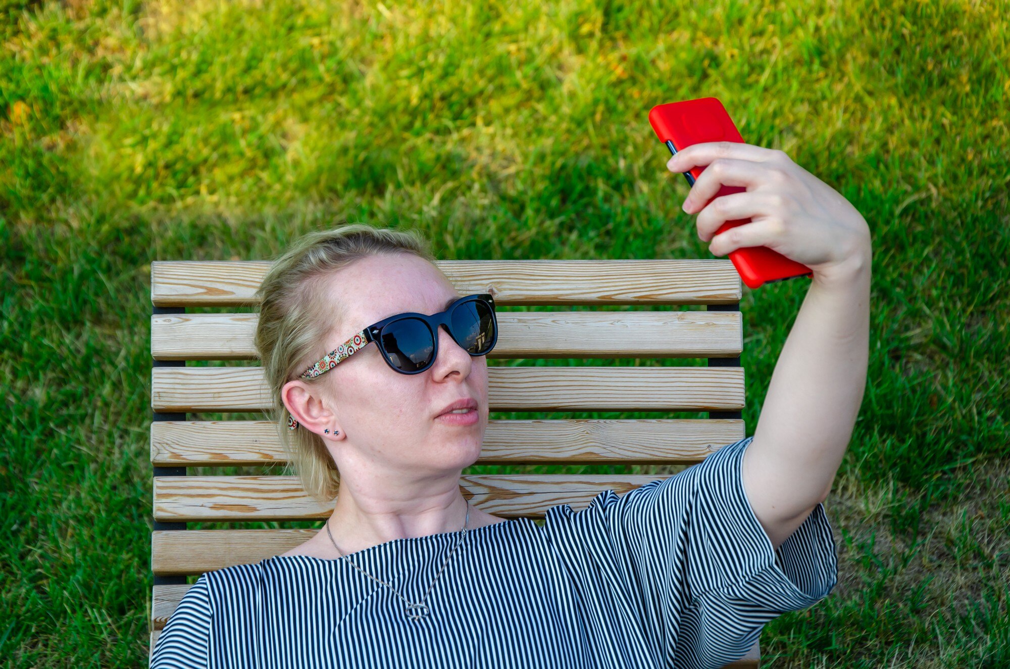 Blondynka robi sobie selfie, robi zdjęcie lub komunikuje się przez wideorozmowę przez telefon w słoneczny dzień w parku