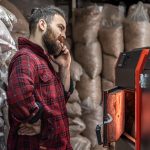 Człowiek w pomieszczeniu z kotłem na paliwo stałe, pracujący na biopaliwo, oszczędne ogrzewanie.