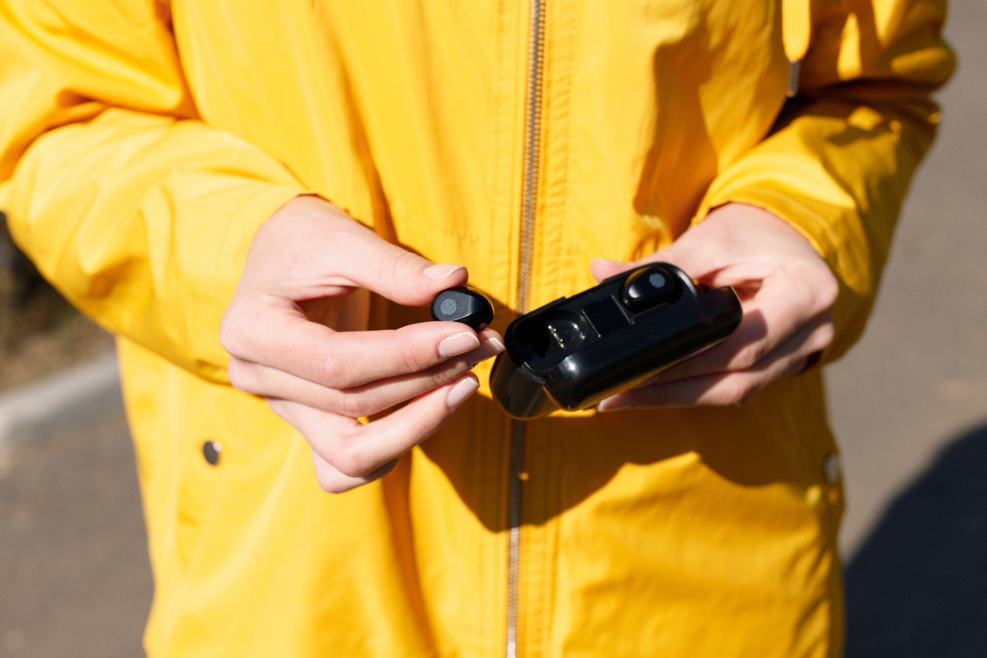 Słuchawki w rękach kobiety w żółtym płaszczu przeciwdeszczowym. zbliżenie
