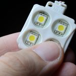 Moduł LED RGB z 4 punktami LED w plastikowej obudowie trzyma palce osoby. zbliżenie