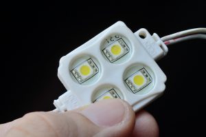 Moduł LED RGB z 4 punktami LED w plastikowej obudowie trzyma palce osoby. zbliżenie