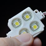 Moduł LED RGB z 4 punktami LED w plastikowej obudowie trzyma palce osoby. zbliżenie