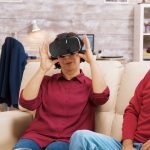 Siostrzeniec uczy babcię korzystania z zestawu do wirtualnej rzeczywistości w salonie