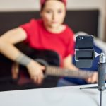 Bliska strzał smartfona na statywie, młoda kobieta nagrywająca się gra na gitarze akustycznej