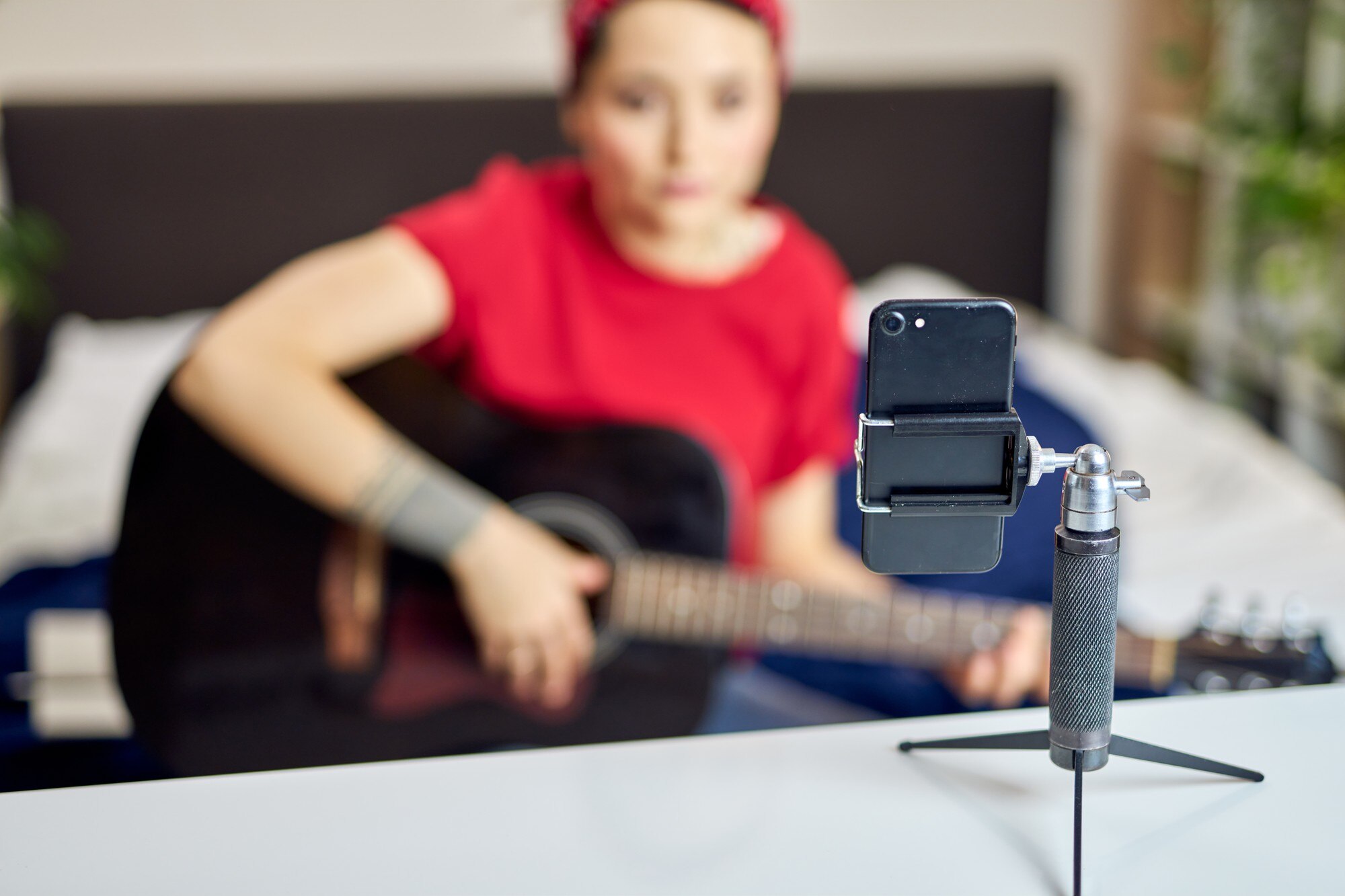 Bliska strzał smartfona na statywie, młoda kobieta nagrywająca się gra na gitarze akustycznej