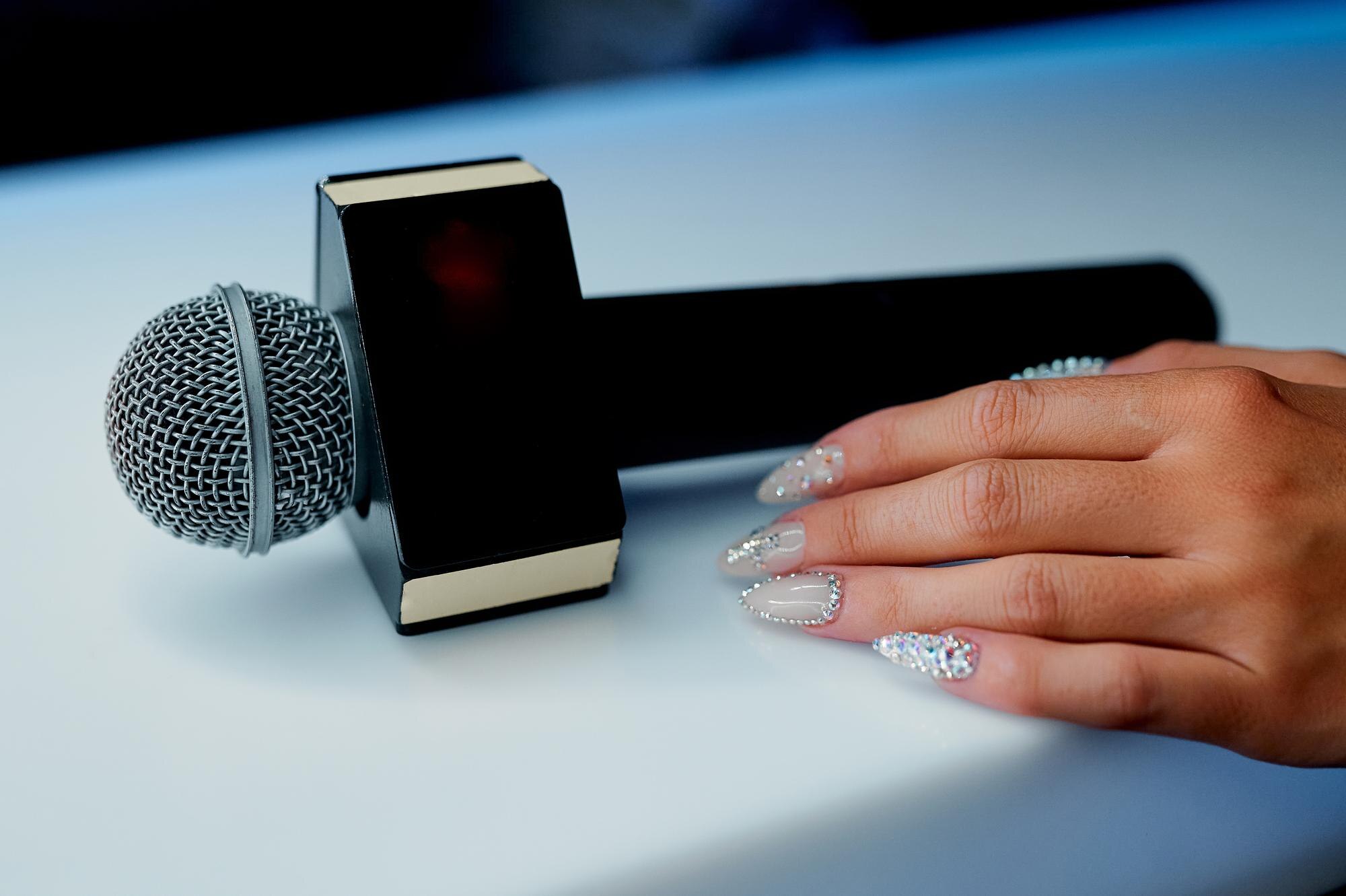Mikrofon na białym stole z pustą płytką na napis obok kobiecej dłoni. Zdjęcie wysokiej jakości