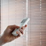 męska ręka trzyma pilota do otwierania drewnianych rolet