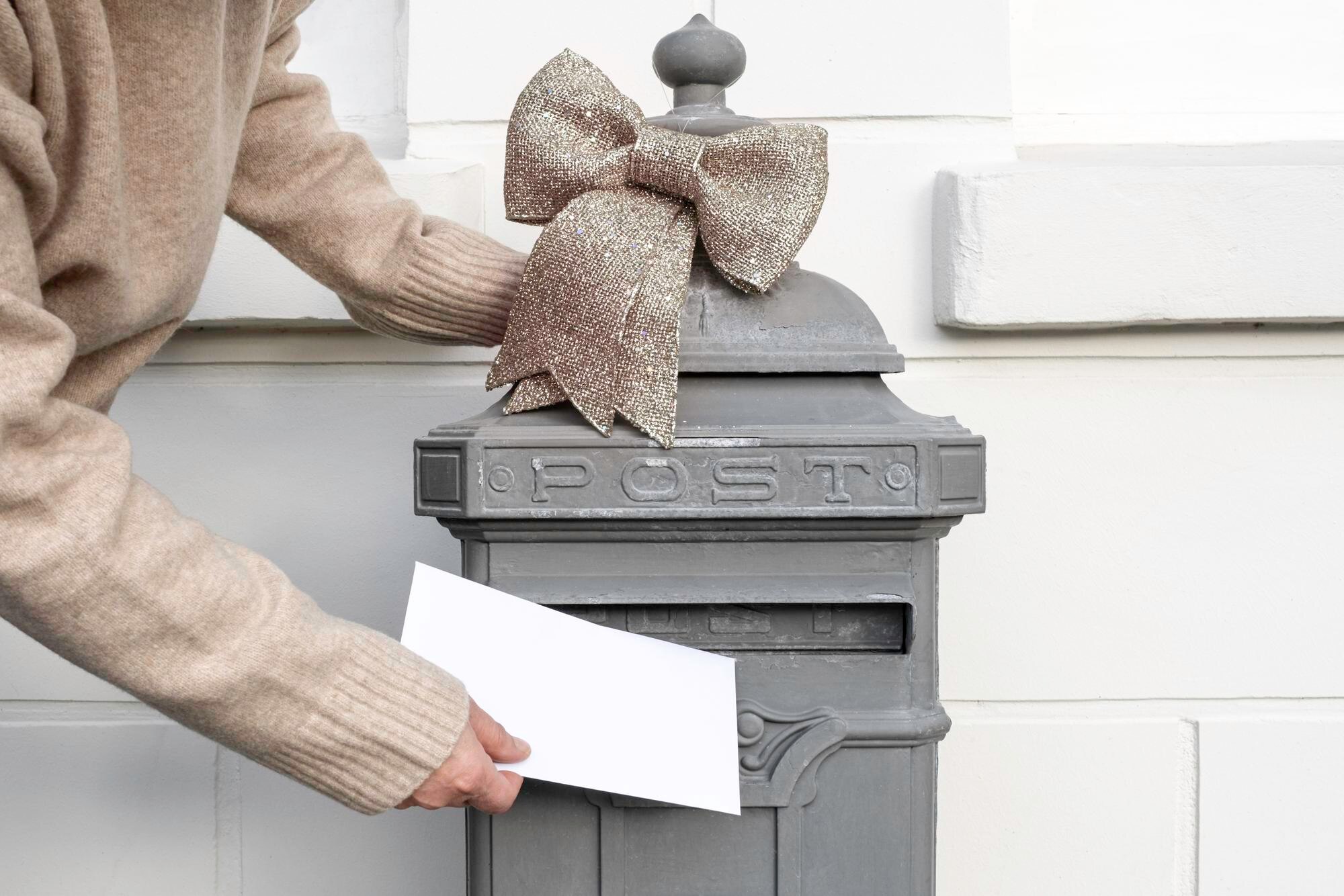 Ręka trzyma list i wkłada do staromodnej skrzynki pocztowej w pobliżu domu, doręczenie na pocztę