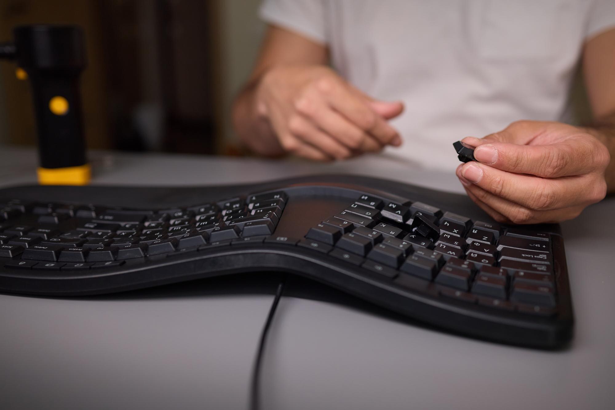 W zbliżeniu widać rękę używającą narzędzia wyciągającego klawisze do skrupulatnego usunięcia klawisza klawiatury