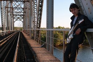 Mężczyzna z gitarą elektryczną w industrialnym krajobrazie na zewnątrz