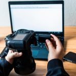 Mężczyzna wkłada baterię do aparatu z laptopem w tle.