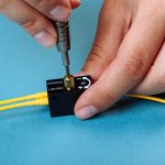 Ręce dostrajają tłumik optyczny Variable za pomocą śrubokręta. Selektywne skupienie. Niebieskie tło.