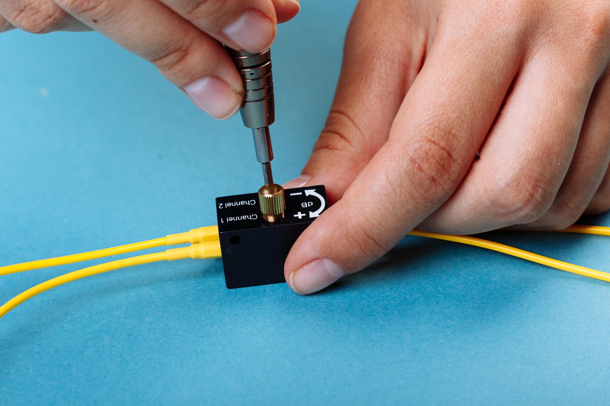 Ręce dostrajają tłumik optyczny Variable za pomocą śrubokręta. Selektywne skupienie. Niebieskie tło.