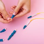 Ręka łączy niebieski tłumik optyczny LC na różowym tle.