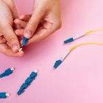 Ręka łączy niebieski tłumik optyczny LC na różowym tle.