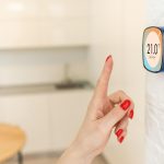 Inteligentny dom cyfrowy termostat dotykowy kobieta dotykająca ekranu dotykowego, aby dostosować temperaturę ogrzewania w ścianie salonu.