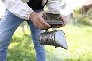 Pszczelarz w kombinezonie ochronnym trzyma palacza w rękach koncepcja narzędzia pszczelarskiego