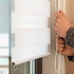 Rolety materiałowe na oknie Mężczyzna otwiera rolety materiałowe