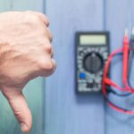 Męska ręka z negatywnym gestem na tle elektronicznego multimetru do pomiaru prądu