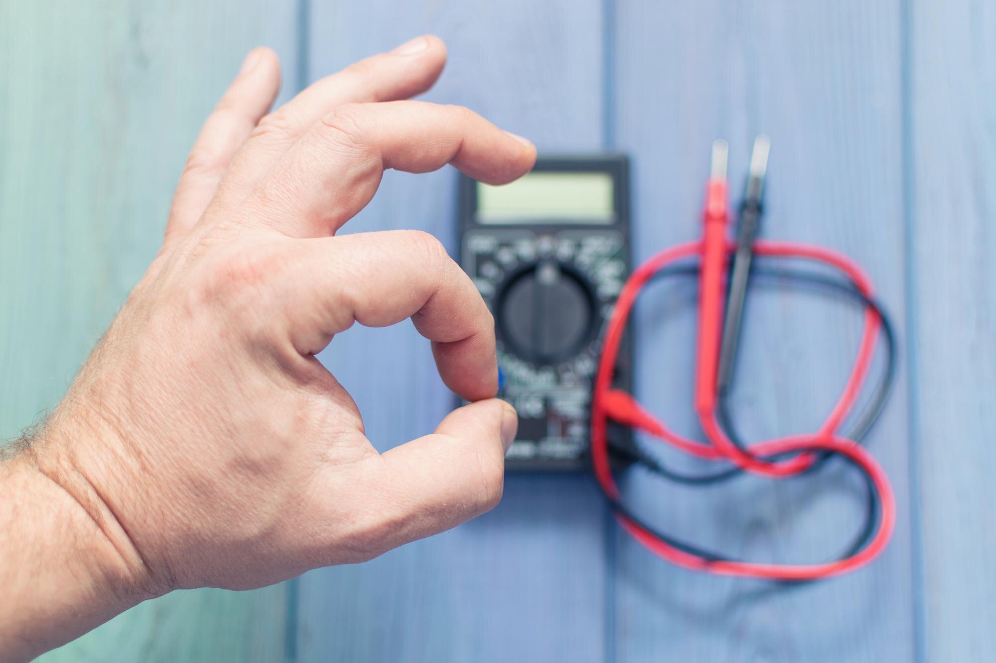 Męska ręka z gestem OK na tle elektronicznego multimetru do pomiaru prądu