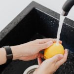 Kobieta opłukująca żółtą cytrynę w zlewie