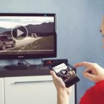 Mężczyzna ze smartfonem podłączonym do telewizora Oglądanie wideo w domu przesyłanie wideo z telefonu na ekran telewizora Nowoczesne gadżety Przesyłanie informacji między urządzeniami przez wifi