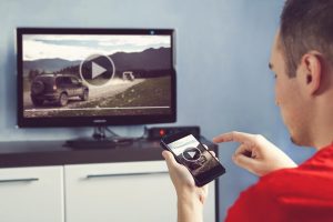 Mężczyzna ze smartfonem podłączonym do telewizora Oglądanie wideo w domu przesyłanie wideo z telefonu na ekran telewizora Nowoczesne gadżety Przesyłanie informacji między urządzeniami przez wifi