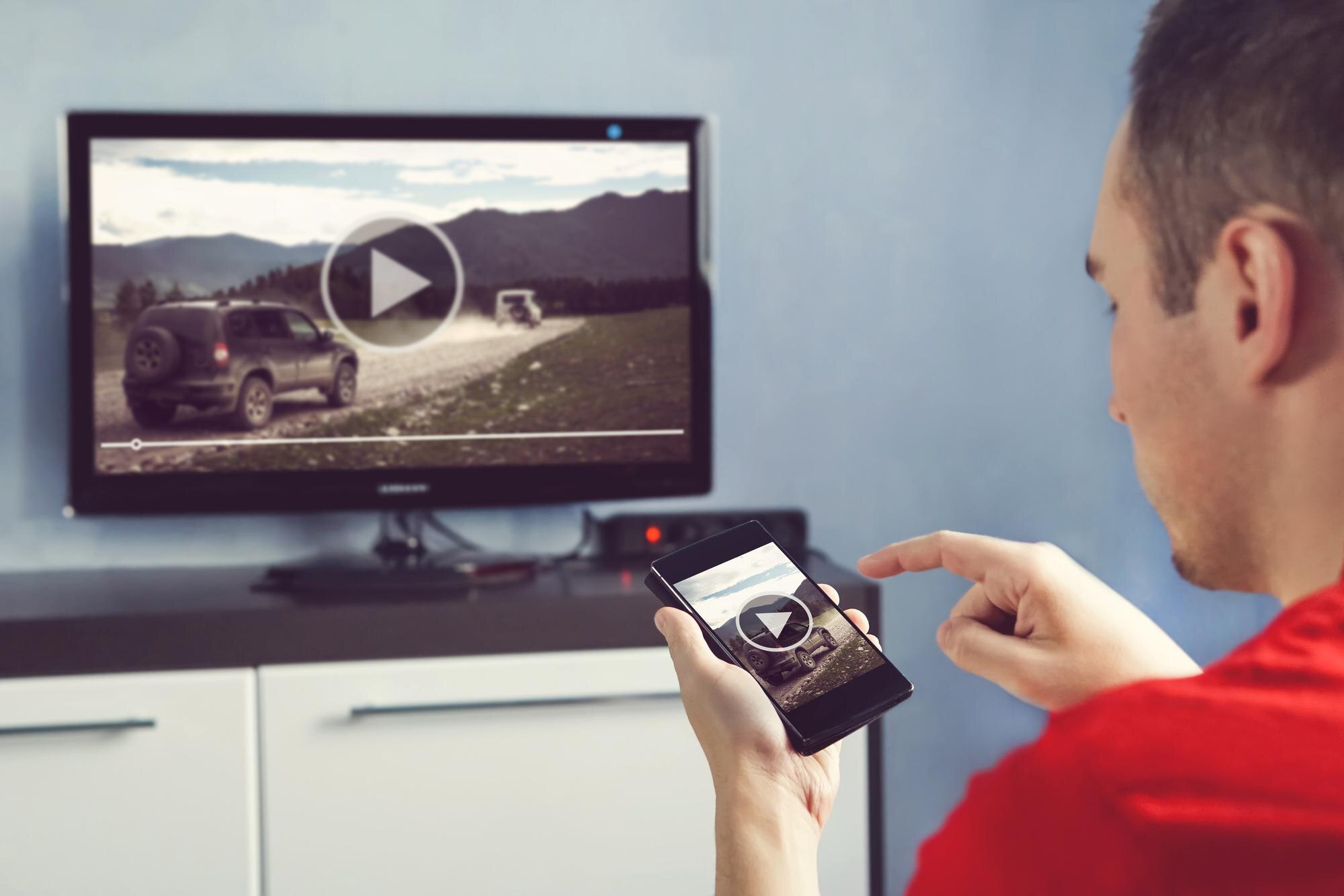 Mężczyzna ze smartfonem podłączonym do telewizora Oglądanie wideo w domu przesyłanie wideo z telefonu na ekran telewizora Nowoczesne gadżety Przesyłanie informacji między urządzeniami przez wifi
