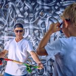 Fajny sportowy dziadek pokazuje deskorolkę zdziwionemu wnukowi w okularach przeciwsłonecznych Starszy mężczyzna pokazuje dziecku, że wiek nie jest przeszkodą w aktywnym sporcie